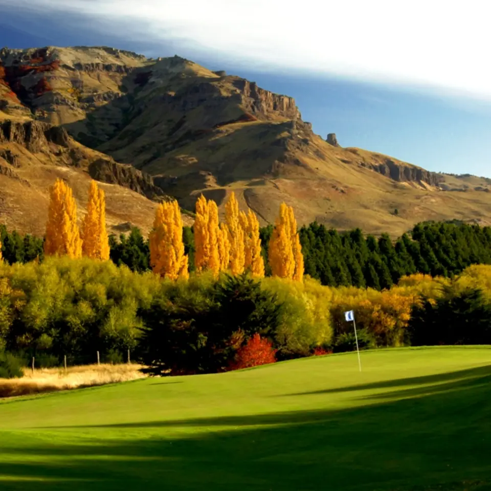 Golden poplars and Andean cliffs behind a green at Chapelco